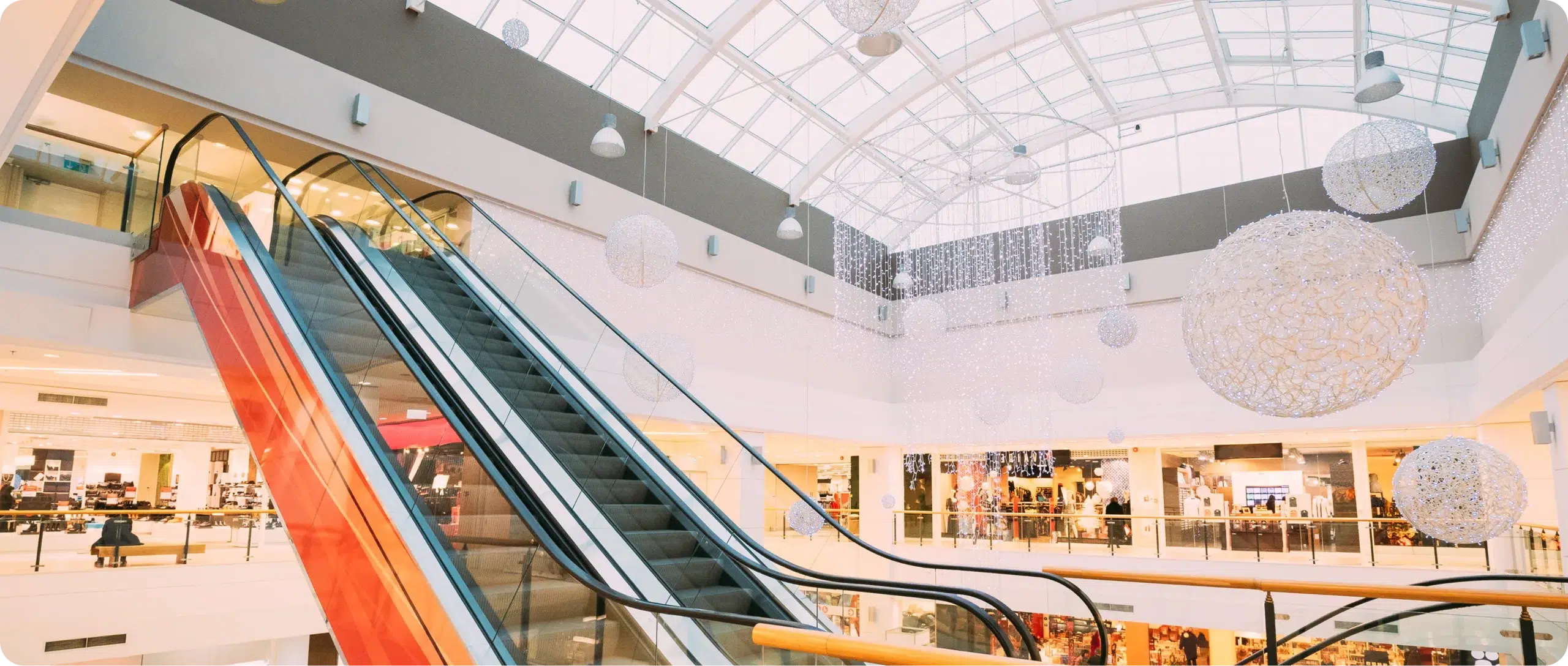 Shopping centre interior with escalators, storefronts and a glass atrium roof